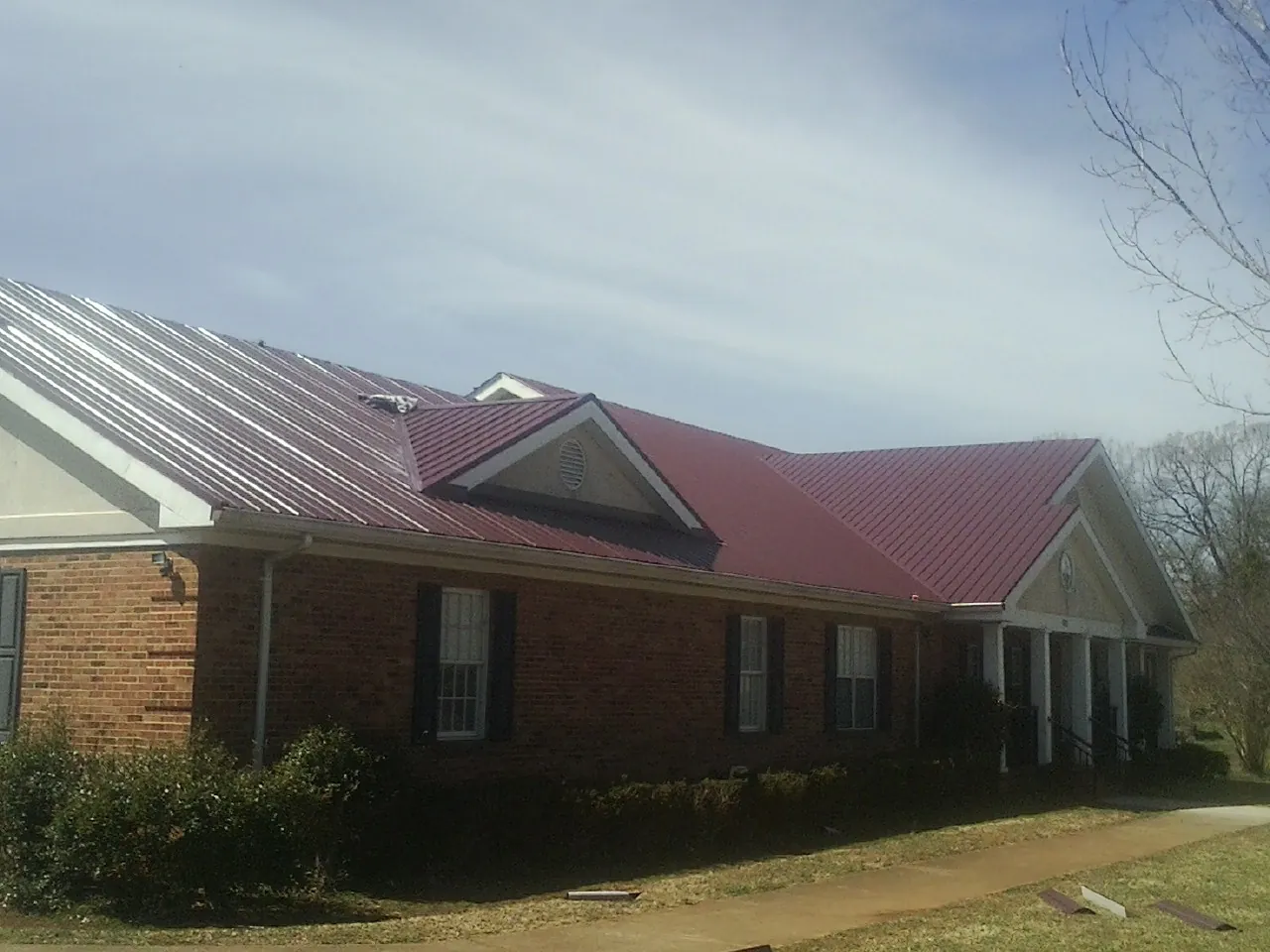 Red metal roof with gabled entries on a long brick building, from a Hail Damage Roof Repair job in Lapeer