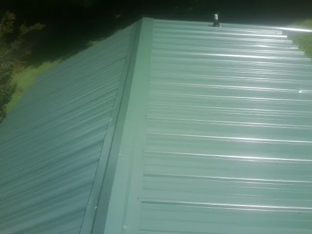 New green metal panels meeting at the ridge of a roof — Flat Roof Repair work by our crew in Lapeer