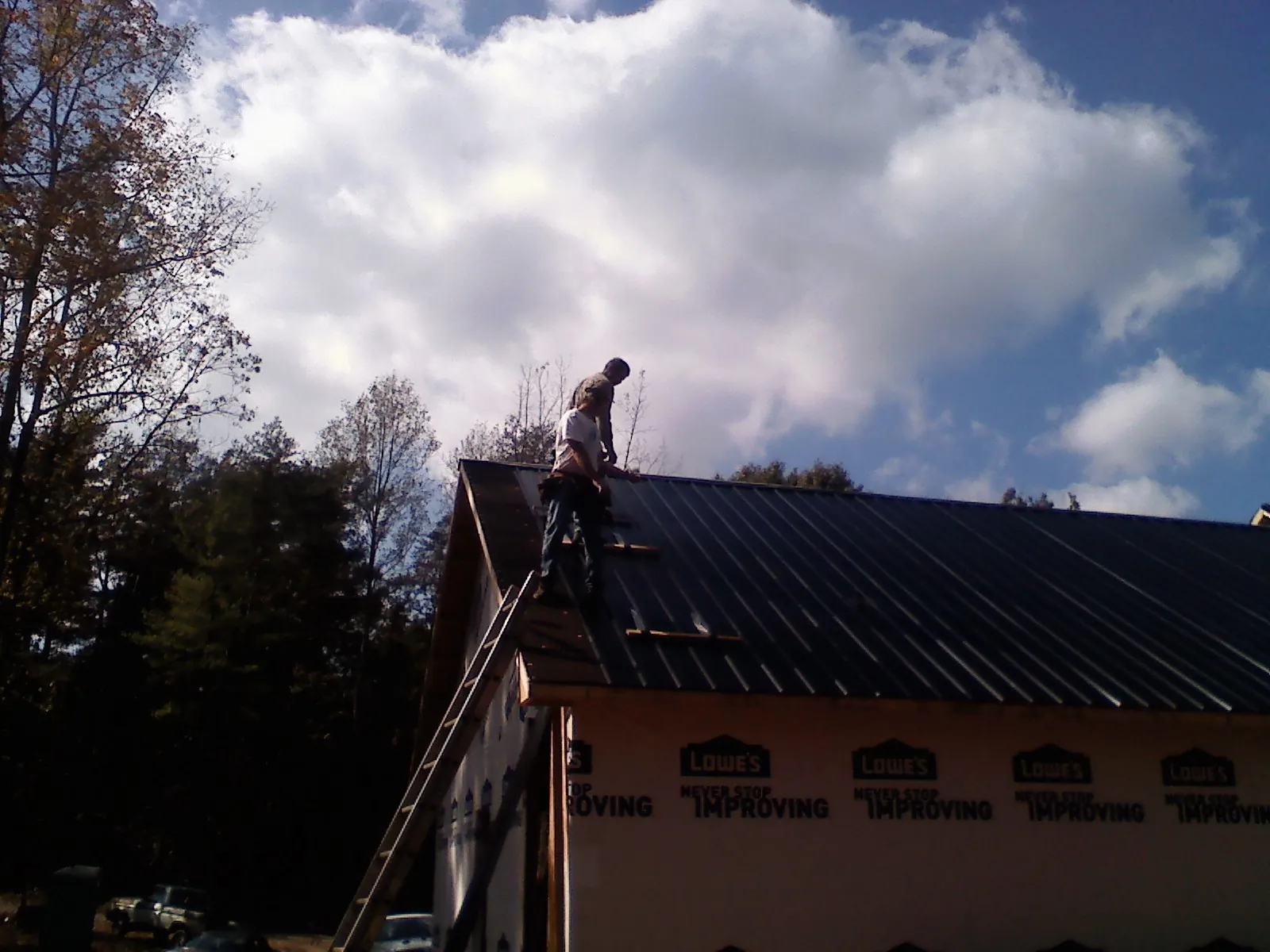 Roofer fastening dark metal panels high against a cloudy sky, from a Roof Inspection job in Lapeer