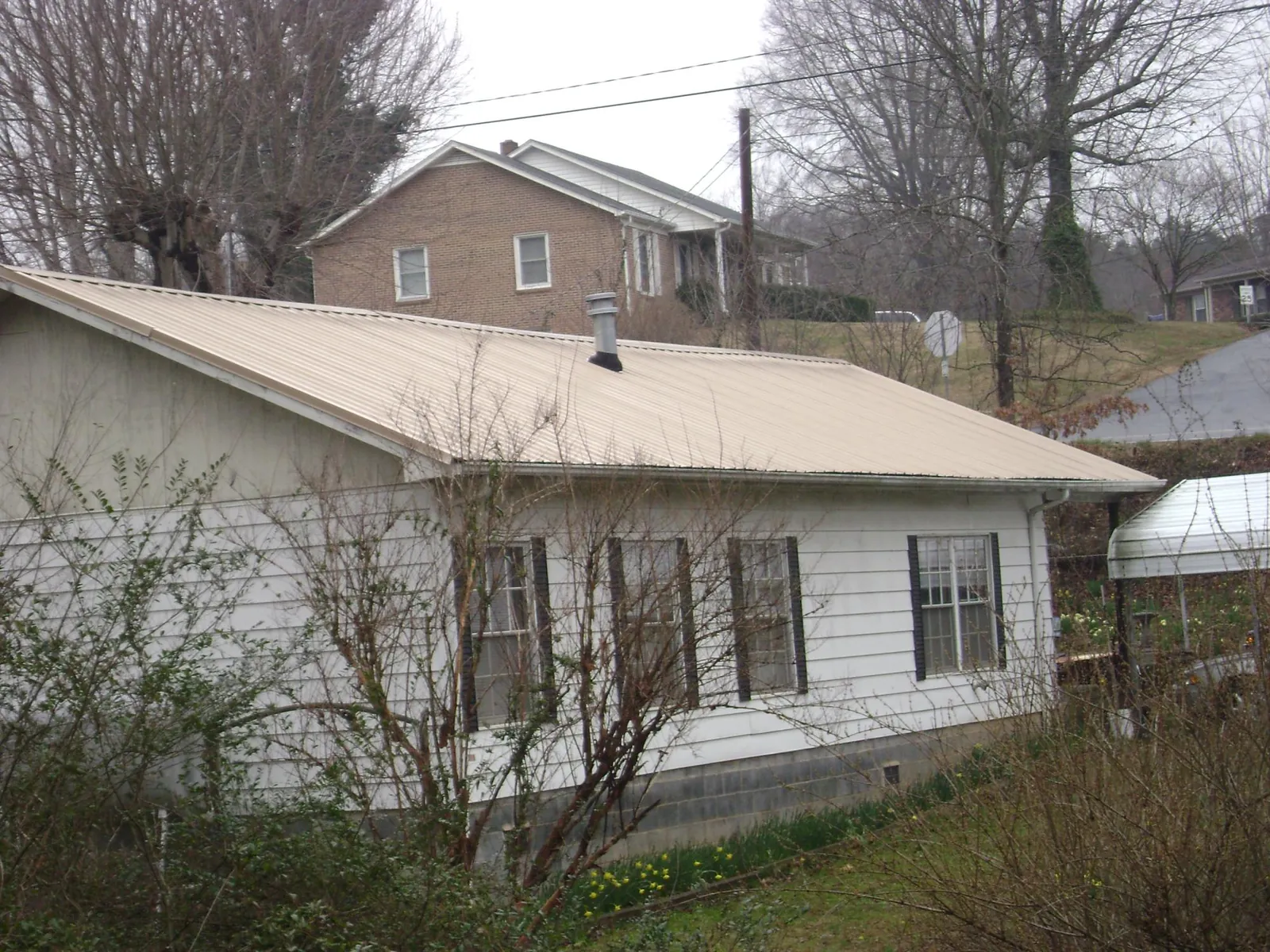 Tan metal roof on a white sided house set into a hillside — Commercial Roofing by Roofing Brothers in Lapeer